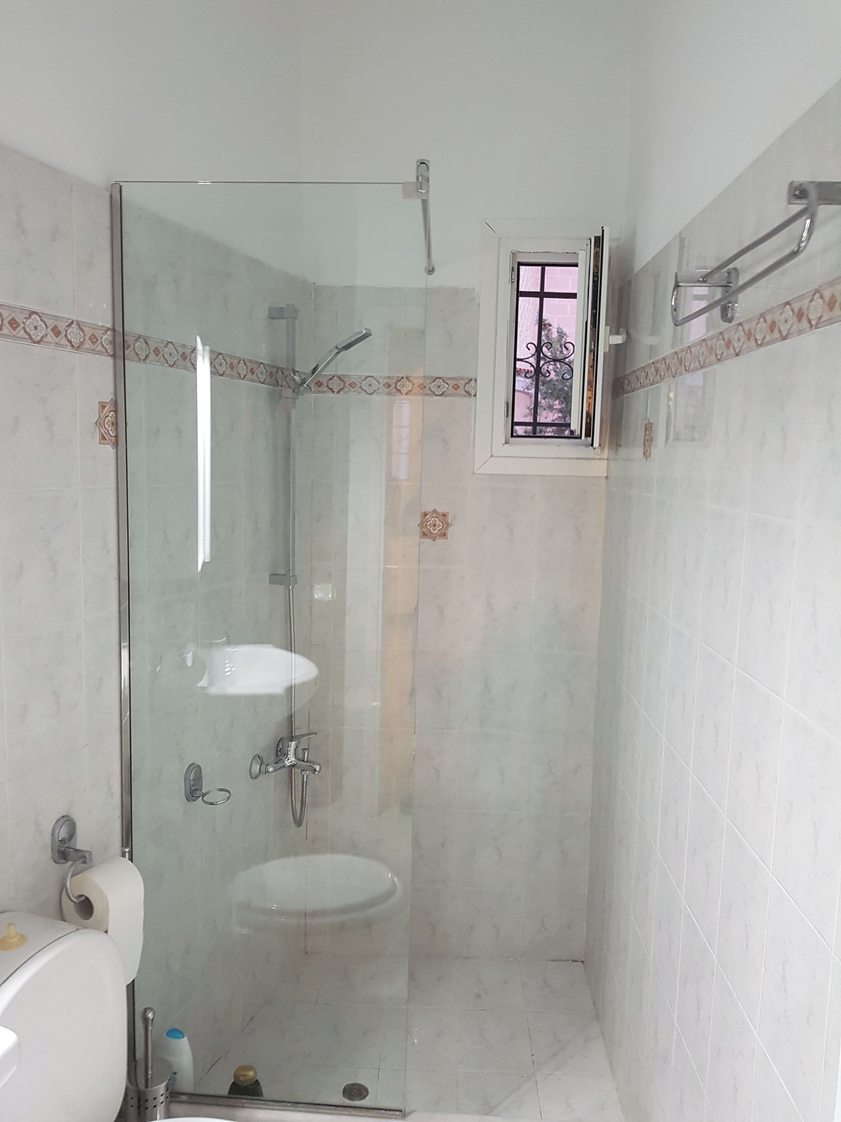 A bathroom with a glass-enclosed shower, a sink, and a window.