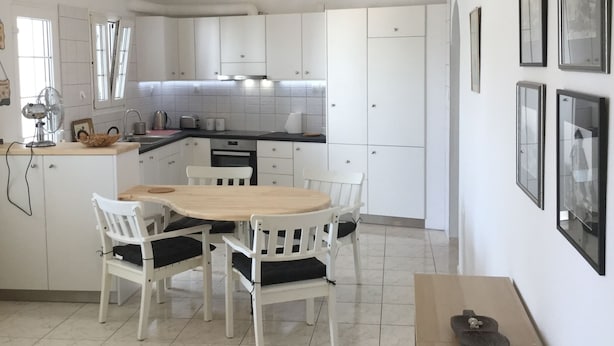 Een moderne keuken met witte kasten, een eettafel met stoelen en een ventilator.