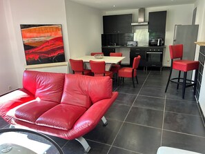 A modern kitchen with dark tiles, a dining area with red chairs, and a red leather sofa. - Country house with 2 apartments, 15 km from Vaison-la-Romaine, with a view of Mont Ventoux, (Travaillan)