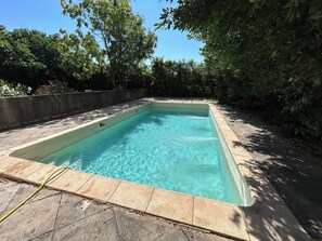 A rectangular swimming pool with clear water, surrounded by a stone deck and bordered by a concrete wall and dense foliage. - Country House 2 apartments 15 kms from Vaison le Romaine facing Mont Ventoux, (Travaillan)
