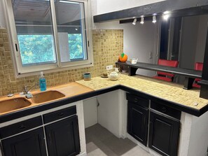 A kitchen with a window, a sink, a countertop, cabinets, and a shelf with a pumpkin and a teapot. - Country house with 2 apartments, 15 km from Vaison-la-Romaine, with a view of Mont Ventoux, (Travaillan)