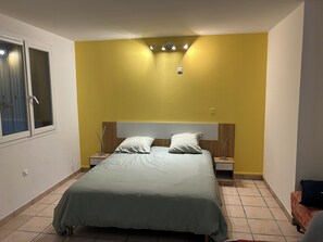 Ein Schlafzimmer mit einem Bett, Nachttischen, einem Fenster und einer gelben Wand.