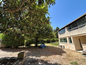 A building with a two-story structure, a tree in the foreground, and a gravel area with some wooden planks. - Country House 2 apartments 15 kms from Vaison le Romaine facing Mont Ventoux, (Travaillan)