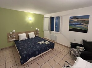 A bedroom with a bed, a nightstand, a chair, a window, and a painting on the wall. - Country house with 2 apartments, 15 km from Vaison-la-Romaine, with a view of Mont Ventoux, (Travaillan)