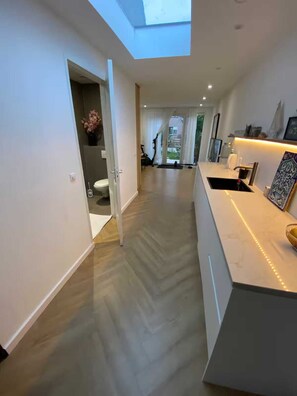 A modern interior with a skylight, a kitchen area with a sink, and a hallway leading to a door. - Family vacation apartment North Sea, nature, fitness & wellness -max 2 adults + 2 children- (Aerdenhout)