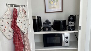 Eine Küche mit Mikrowelle, Toaster, Kaffeemaschine und Gläsern auf Regalen.