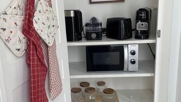 A kitchen with a microwave, toaster, coffee maker, and jars on shelves.