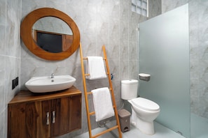 A bathroom with a wooden vanity, a round mirror, a toilet, and a shower area.