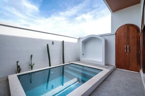 A swimming pool with a clear blue water, a wooden door, and a white wall with a small plant.
