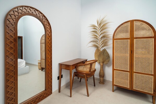 A room with a wooden desk, a chair, a large mirror, and a rattan cabinet.