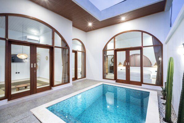 A modern indoor pool area with glass doors, a small pool, and a ceiling skylight.