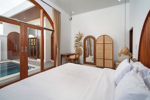 A hotel room with a large bed, a desk, a chair, a pool view, and wooden furniture.