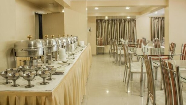 A dining area with multiple tables and chairs, a buffet setup with various dishes and utensils, and a neutral color scheme. - HOTEL ORCHARD (Pune)