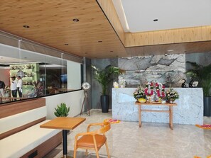 A modern reception area with a marble counter, wooden benches, and potted plants. - Euro Hotel (Patancheruvu)