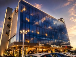 A modern hotel building with a glass facade, labeled 'Euro Hotel,' featuring a prominent entrance and a visible parking area. - Euro Hotel (Patancheruvu)