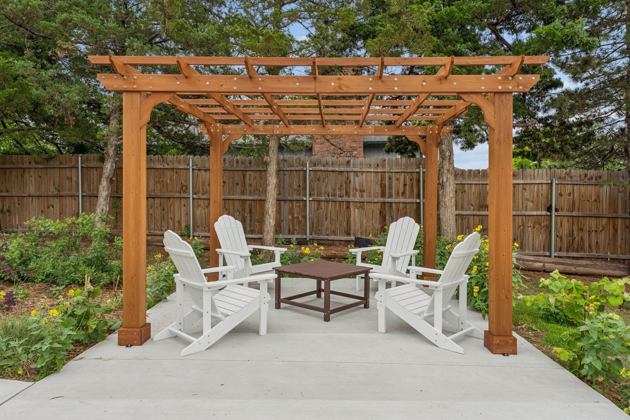 Eine Holz-Pergola mit Tisch und zwei Adirondack-Stühlen in einem Garten.