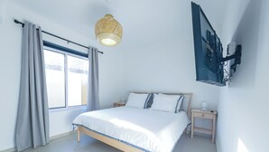 A bedroom with a bed, curtains, a bedside table, a wall-mounted TV, and a window. -  Villa Sweet, private pool & garden, 3 bedrooms, sleeps up to 8 guests (Oranjestad)