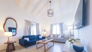A modern living room with a blue sofa, a wooden coffee table, a TV mounted on the wall, and a large mirror. -  Villa Sweet, private pool & garden, 3 bedrooms, sleeps up to 8 guests (Oranjestad)