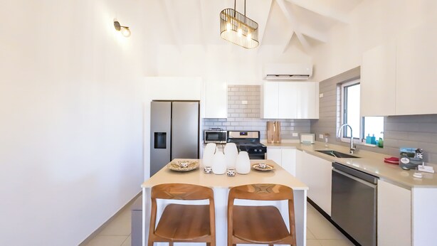 A modern kitchen with a central island, white cabinetry, stainless steel appliances, and a hanging light fixture. -  Villa Sweet, private pool & garden, 3 bedrooms, sleeps up to 8 guests (Oranjestad)