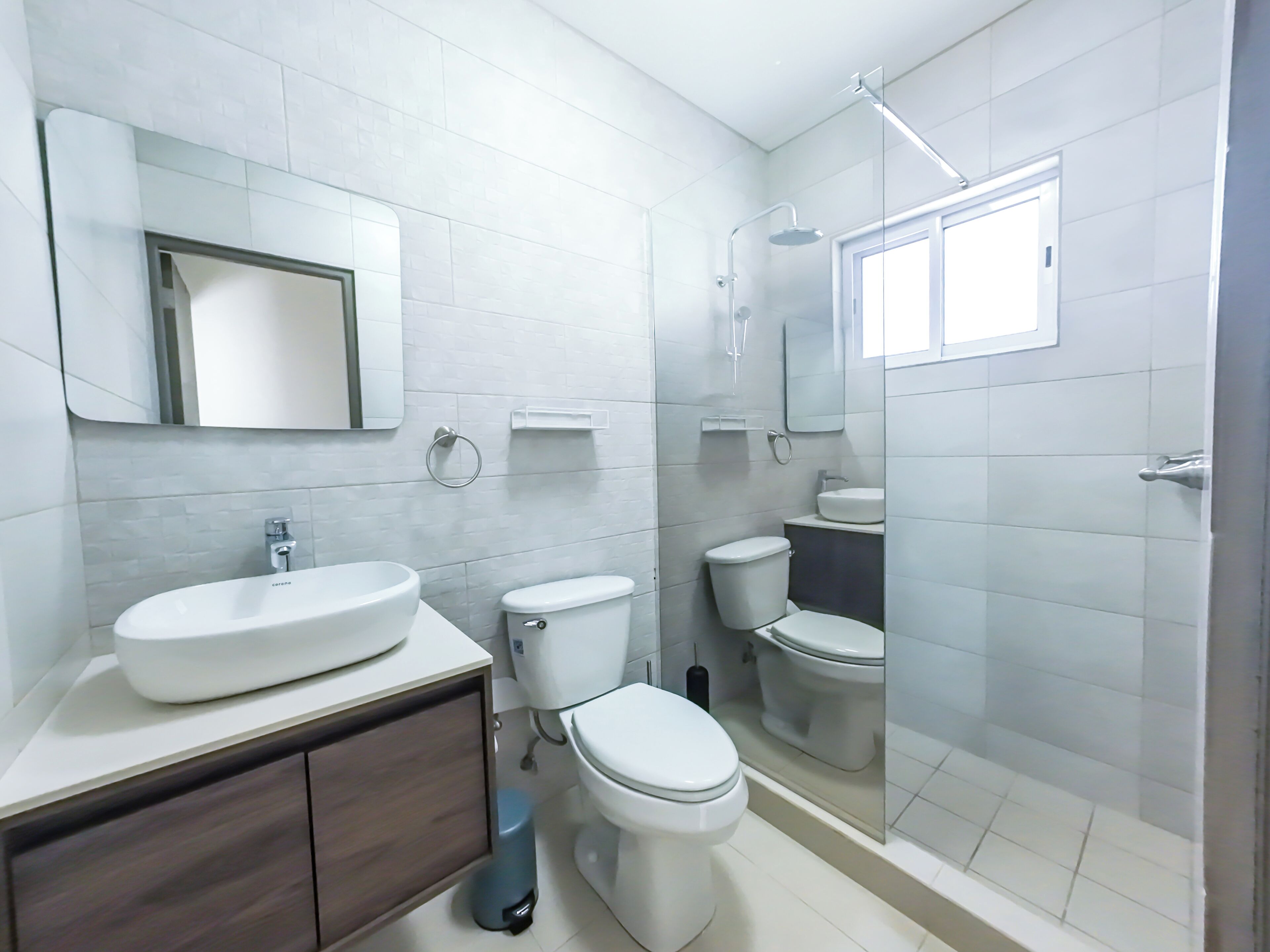 Une salle de bain moderne avec un grand lavabo, deux toilettes, une douche et un miroir.