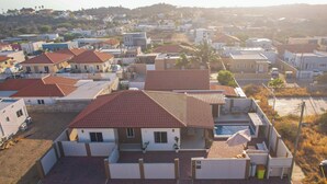 A residential area with houses featuring red-tiled roofs, a swimming pool, and a paved driveway. -  Villa Sweet, private pool & garden, 3 bedrooms, sleeps up to 8 guests (Oranjestad)