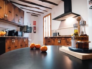 Une cuisine avec des meubles de rangement en bois, un four à micro-ondes et une planche à découper en bois sur laquelle on voit des oranges et une bouteille.
