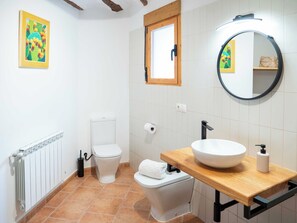 A bathroom with a toilet, sink, mirror, and a framed picture on the wall. - Vrbo Property (La Gila,Alcalá del Júcar)