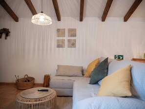 A living room with a light-colored sofa, a round wicker ottoman, a hanging light fixture, and four wall-mounted artworks.