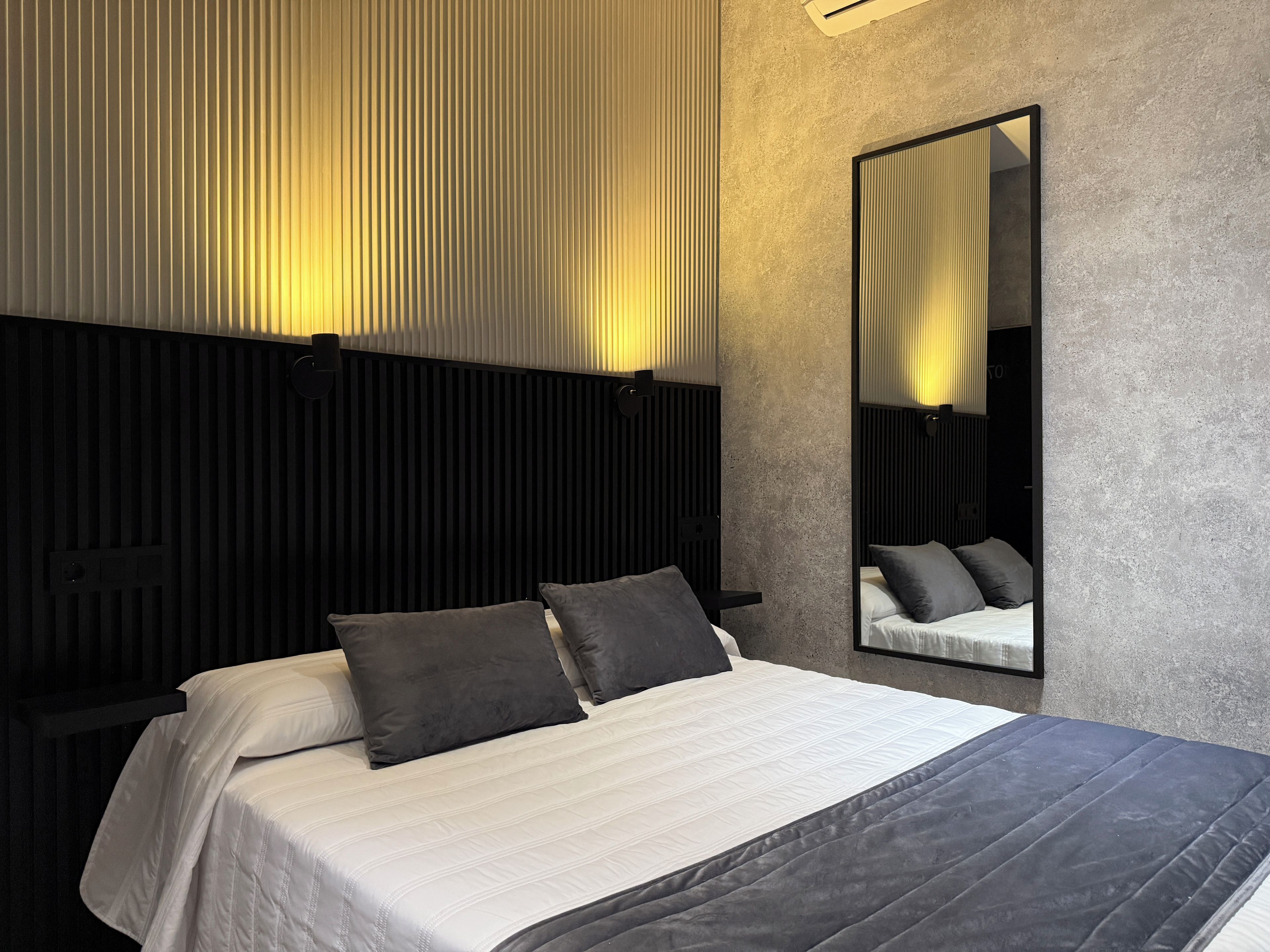 Habitación de hotel moderna con una cama grande, cabecera con listones verticales, espejo montado en la pared y pared con textura.