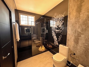 A modern bathroom with a glass-enclosed shower, a large mirror, and a leopard mural on the wall.