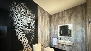 Un baño moderno con un gran mural en la pared de un leopardo de las nieves, un inodoro blanco, un bidé y un tocador con espejo.