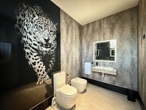 A modern bathroom with a large wall mural of a snow leopard, a white toilet, a bidet, and a vanity with a mirror.
