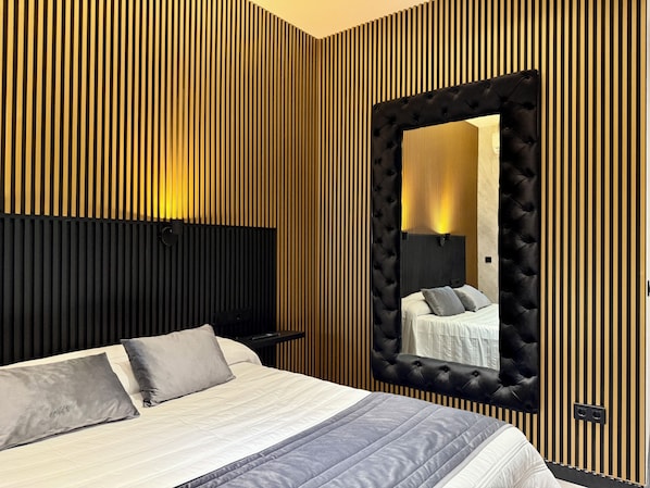 A modern bedroom with a large bed, a headboard, a mirror, and a wall with vertical wooden slats.