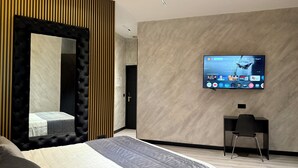 Una habitación de hotel moderna con una cama grande, un televisor montado en la pared, un escritorio y un espejo con listones de madera verticales.