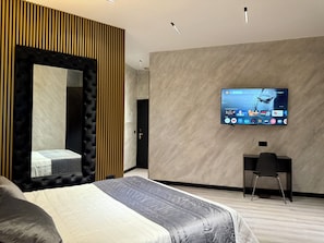 Una habitación de hotel moderna con una cama grande, un televisor montado en la pared, un escritorio y un espejo con listones de madera verticales.