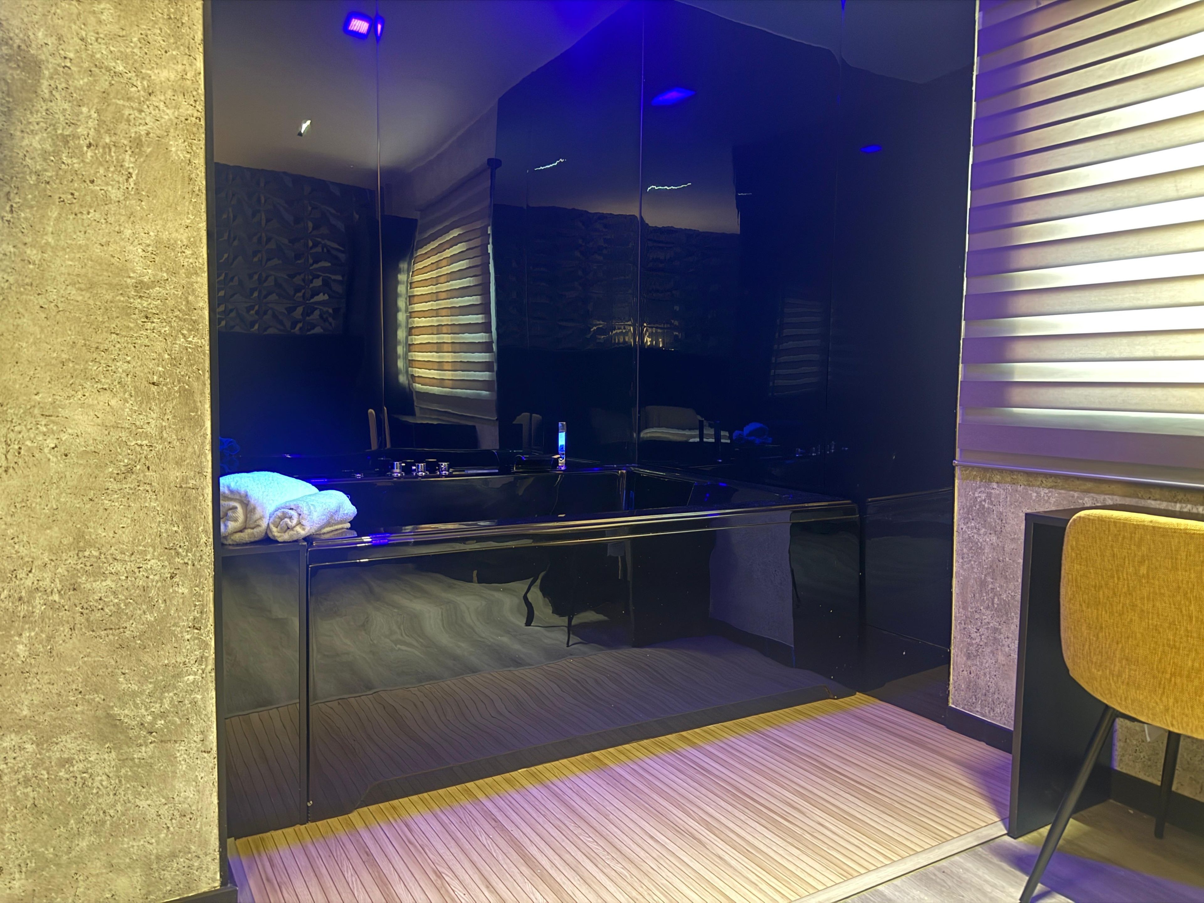 Une chambre moderne avec un lit, une petite table et une chaise. Il y a une fenêtre avec des stores, et la chambre est dotée d’un plancher en bois.