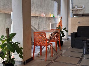 A modern interior with a concrete accent wall, a table with chairs, a black sofa, and potted plants. - Aviora Residencies Gachibowli  (Hyderabad)
