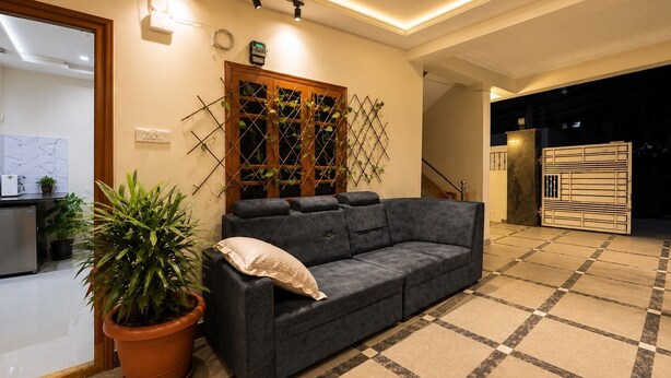 A modern living room with a grey sofa, a potted plant, a wooden lattice wall, and a tiled floor. - Aviora Residencies Gachibowli  (Hyderabad)