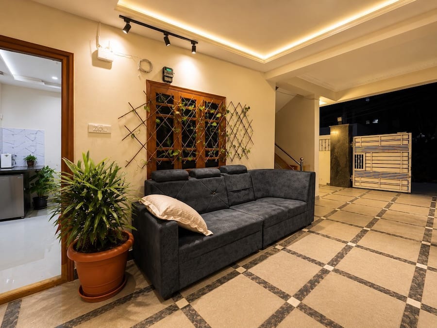 Una sala de estar moderna con un sofá gris, una planta en maceta, un muro de celosía de madera y un piso de baldosas.