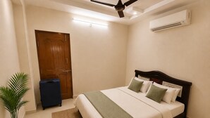 A bedroom with a bed, a ceiling fan, an air conditioner, a door, a suitcase, and a potted plant. - Aviora Residencies Gachibowli  (Hyderabad)