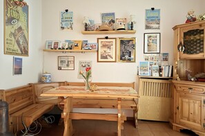 Una habitación acogedora con un banco de madera, una mesa con un jarrón de flores y estantes con objetos varios y cuadros enmarcados.