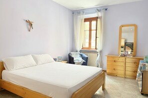 Un dormitorio con cama de madera, una silla, cómoda, espejo y ventana con cortinas.