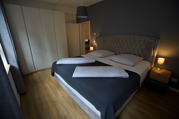 Une chambre à coucher comprenant un lit, des lampes de chevet, une armoire et une porte donnant sur une autre pièce.