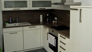 Una cucina moderna con mobili bianchi, forno integrato, macchina del caffè e cappa aspirante in acciaio inossidabile.