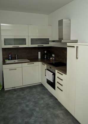 Una cocina moderna con armarios blancos, horno empotrado, cafetera y extractor de acero inoxidable.