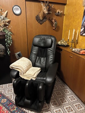 Un fauteuil de massage avec une couverture, une porte en bois ornĂ©e dâune tĂȘte de cerf et une petite statue de Bouddha.