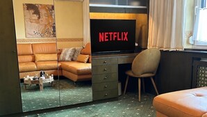 Una sala de estar moderna con un sofá de cuero, una mesa de centro de madera con bebidas, un escritorio con televisor Netflix y un espejo grande.