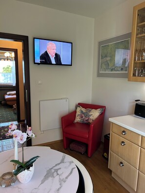 Une pièce avec un téléviseur, un fauteuil rouge, une table en marbre et un meuble.
