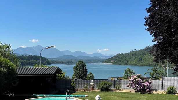 Una piscina con vistas a un lago y montañas, rodeada por un césped cuidado y flores.