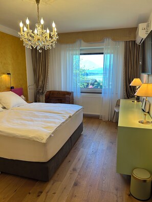 A hotel room with a large bed, a desk, a chair, a chandelier, and a view of the outdoors. - Golden Rooms Exclusive, apartment for 2 adults and 1 child (Völkermarkt)